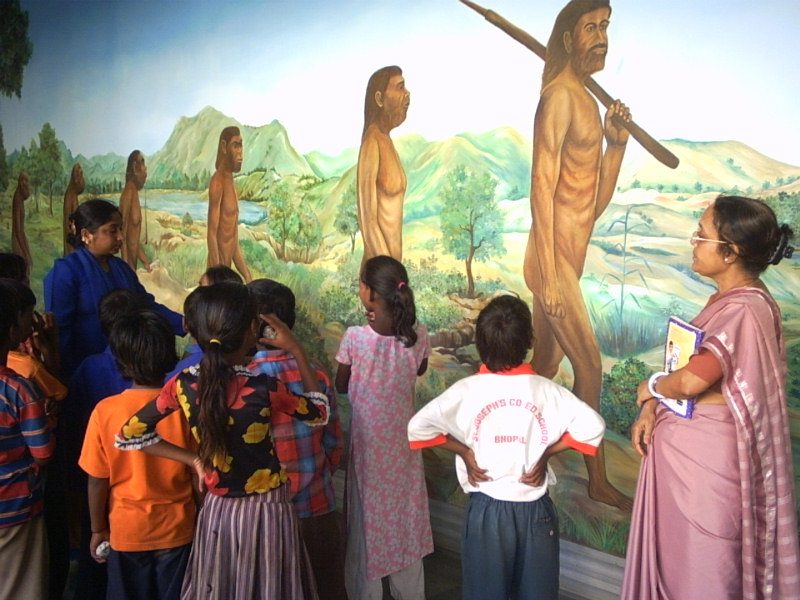 Children studying a mural of human evolution with their teacher at the Regional Museum of Natural History